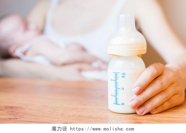 褐色木质桌子母亲抱着婴儿奶瓶与前景母乳喂养母乳